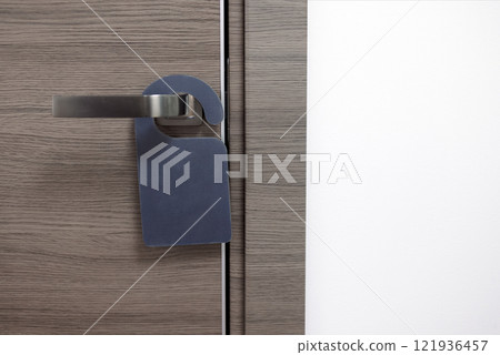 Close-up of a closed wooden door of a hotel room with an empty black sign. The layout of the sign on the modern door handle. Close-up of a closed wooden door of a hotel room with an empty black sign. The layout of the sign on the modern door handle. 121936457