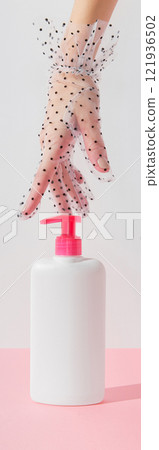 Womans hand touch white bottle on pastel pink and white background. Self care concept Womans hand touch white bottle on pastel pink and white background. Self care concept 121936502