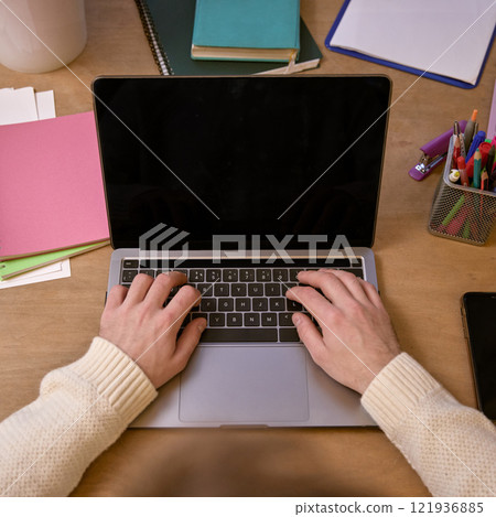 Close-up of hands typing on a laptop in a workspace with colorful stationery and a calculator, depicting a productive office environment. Front view 121936885