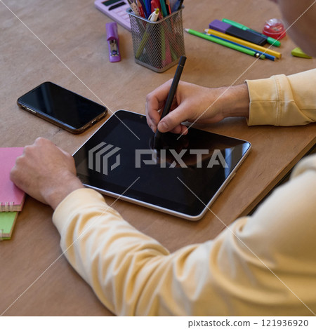 Close-up of person sketching on tablet wit stylus at desk surrounded by colorful stationery and smartphone Close-up of person sketching on tablet wit stylus at desk surrounded by colorful stationery and smartphone 121936920
