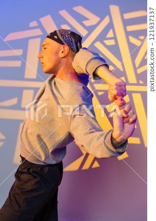 A young man in a bandana dances against a wall with geometric patterns projected on it A young man in a bandana dances against a wall with geometric patterns projected on it 121937137