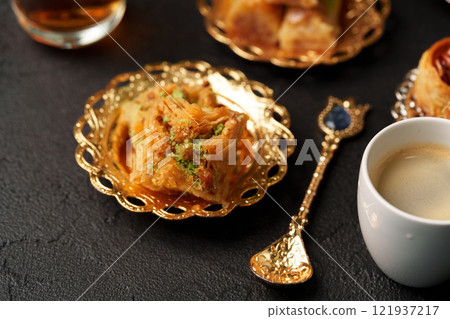 Delightful dessert with sweet pastries and coffee served in golden bowls on a dark table Delightful dessert with sweet pastries and coffee served in golden bowls on a dark table 121937217