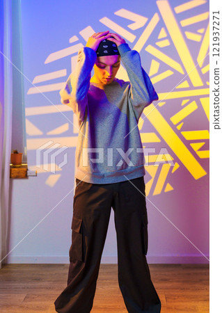 A young person stands with their hands on their head, looking down, in front of a wall with a projected pattern 121937271