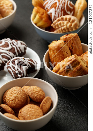 Assorted baked goods arranged in bowls on a dark surface for a delightful snack experience 121937273