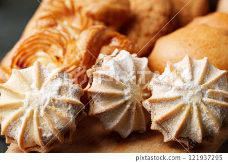 Delicious assortment of freshly baked pastries and meringues displayed on a wooden board in a cozy kitchen setting 121937295