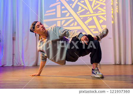 A dancer performs a breakdancing move in a studio with white curtains and a geometric light projection on the wall 121937360