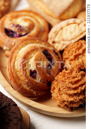 Assortment of freshly baked pastries on a wooden platter at a cozy bakery setting in the morning light Assortment of freshly baked pastries on a wooden platter at a cozy bakery setting in the morning light 121937578
