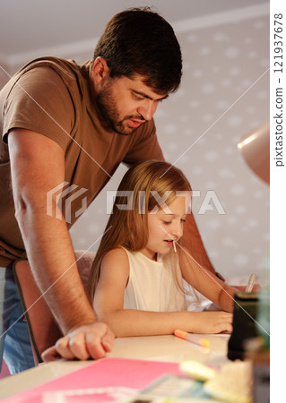 A father helps his daughter with her homework at home 121937678