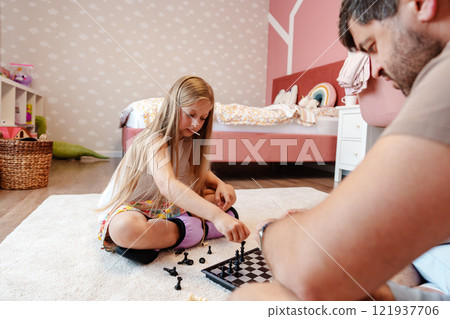 A young girl plays chess with her father in their home A young girl plays chess with her father in their home 121937706