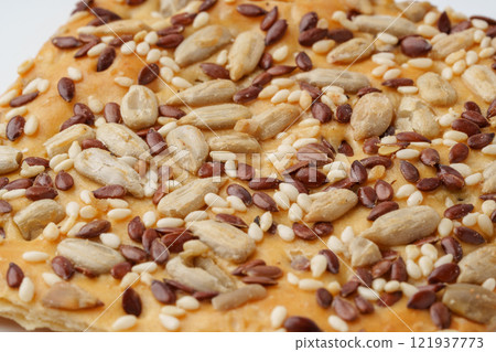 Delicious crispy snack topped with a blend of seeds and nuts on a white plate in bright lighting Delicious crispy snack topped with a blend of seeds and nuts on a white plate in bright lighting 121937773