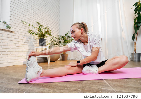 A woman stretches her leg while exercising on a pink yoga mat 121937796