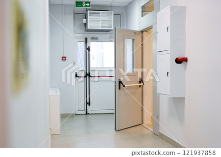 Interior corridor with an open door leading to an exit in a modern building 121937858