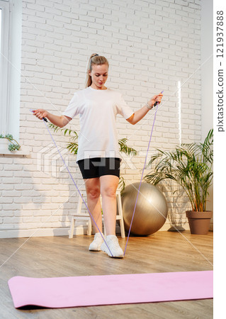 A woman skipping rope in a bright living room filled with plants 121937888