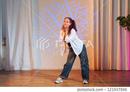 A young woman dances in a studio with a geometric pattern projected on the wall behind her A young woman dances in a studio with a geometric pattern projected on the wall behind her 121937898