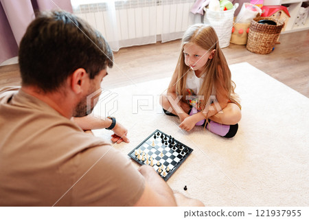 A father and daughter play chess on the floor at home 121937955