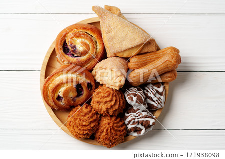 Assorted sweet pastries and baked goods on a wooden plate arranged for dessert enjoyment 121938098