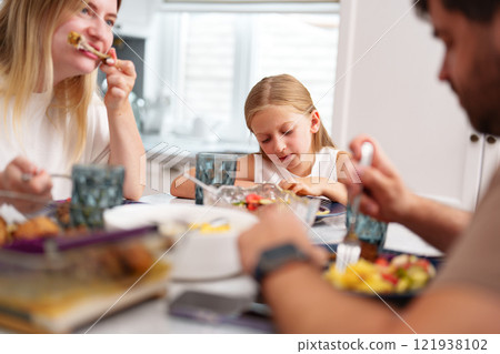 A family enjoys a meal together at a kitchen table A family enjoys a meal together at a kitchen table 121938102
