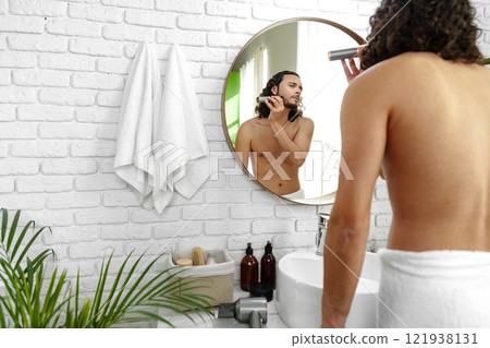 A man with curly hair grooming himself in the bathroom while looking into a round mirror A man with curly hair grooming himself in the bathroom while looking into a round mirror 121938131