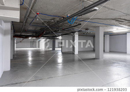 Empty underground parking garage with exposed pipes and clean concrete floors in a modern structure 121938203