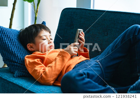 Elementary school boy lying on the sofa and using a smartphone 121938241