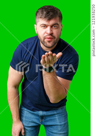 A man blowing a kiss while standing against a bright green backdrop in a casual outfit A man blowing a kiss while standing against a bright green backdrop in a casual outfit 121938250
