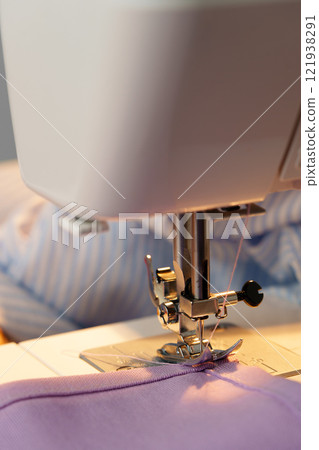 Sewing machine in use on a wooden table, stitching a light fabric in a well-lit indoor workspace 121938291