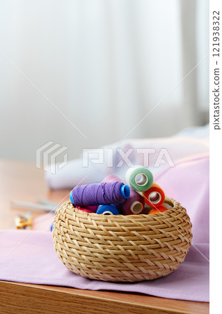 A woven basket filled with colorful sewing threads on a wooden table 121938322