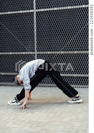 A person stretches in front of a chain link fence, reaching their hands down to touch the pavement 121938341