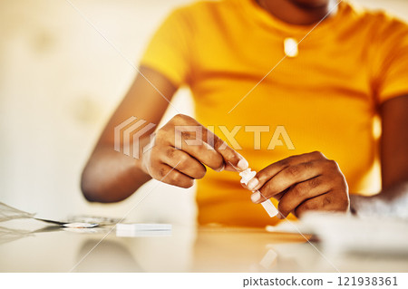 Hands of African female with HIV and Aids at home blood self test kit sitting at a desk waiting to check for results. Closeup of young afro woman with medicine or pills for a medical condition. 121938361