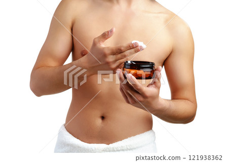A young man applying skincare cream on his face with a focused expression, demonstrating personal grooming at home 121938362