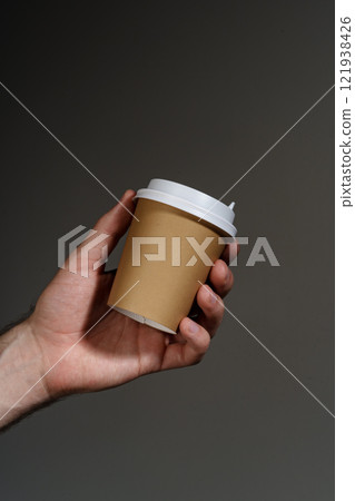 A hand holding a disposable coffee cup against a dark background A hand holding a disposable coffee cup against a dark background 121938426