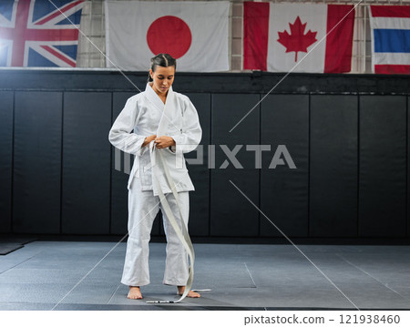 Professional karate student dressing and prepare for practice in a dojo or club. Female mix martial art athlete tying belt in training for a fight, competition or exercise workout in a sport studio 121938460