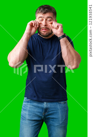 Man expressing frustration with tired eyes while standing in front of a bright green background 121938541