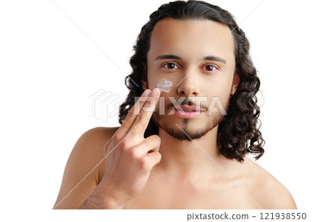 A young man demonstrates skincare routine with moisturizer on his face A young man demonstrates skincare routine with moisturizer on his face 121938550