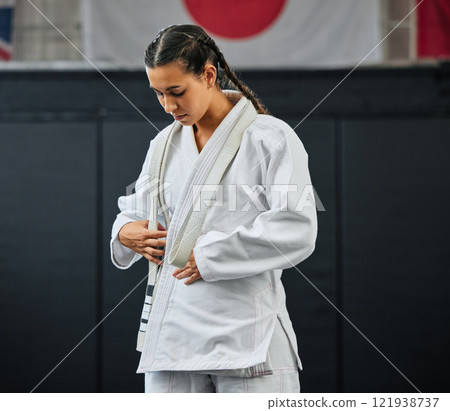 Mma, karate and self defense with a young woman getting ready in her gi or uniform for training, exercise and practice. Workout, sport and fighting with a female athlete standing in a gym or studio Mma, karate and self defense with a young woman getting ready in her gi or uniform for training, exercise and practice. Workout, sport and fighting with a female athlete standing in a gym or studio 121938737