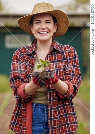 Sustainable farmer holding a plant or seedling outdoors smiling and happy about her organic farm or garden. Young female nature activist that is passionate about sustainability standing on farmland 121938790