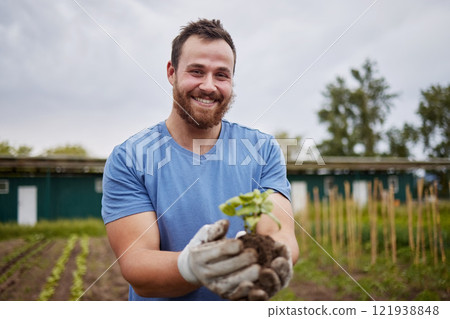 Happy farming worker with a plant on an agriculture farm with a smile. Farmer advertising sustainability, growth and ecology on a green field or land in a nature eco friendly environment countryside Happy farming worker with a plant on an agriculture farm with a smile. Farmer advertising sustainability, growth and ecology on a green field or land in a nature eco friendly environment countryside 121938848