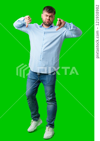 Man expressing disapproval with thumbs down gesture against a bright green background Man expressing disapproval with thumbs down gesture against a bright green background 121938982