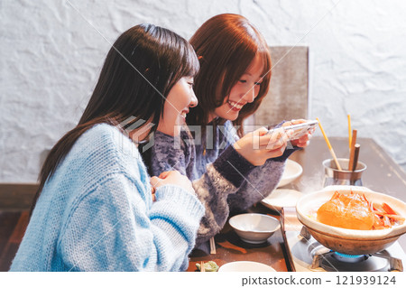Two young women taking pictures of the beautiful crab hotpot with their smartphones [Photo courtesy of Seafood Izakaya Gyoruko] 121939124
