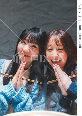 Two young women saying "Itadakimasu" in front of a crab hotpot [Photo courtesy of Seafood Izakaya Gyoruko] 121939179
