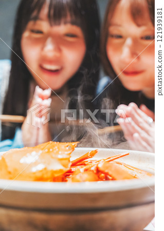 Two young women saying "Itadakimasu" in front of a crab hotpot [Photo courtesy of Seafood Izakaya Gyoruko] 121939181