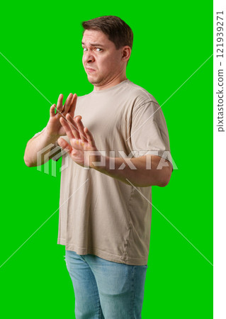 A man with a neutral expression gestures defensively against a bright green background 121939271