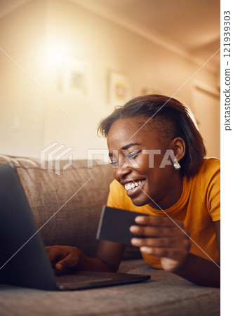 Online shopping young, happy and smiling African lady with bank, credit or gift card. Excited, comfortable and cheerful female typing on laptop searching, browsing and buying present from home. Online shopping young, happy and smiling African lady with bank, credit or gift card. Excited, comfortable and cheerful female typing on laptop searching, browsing and buying present from home. 121939303