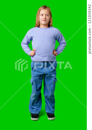 Child wearing a blue sweater and light blue pants stands confidently in front of a green background Child wearing a blue sweater and light blue pants stands confidently in front of a green background 121939342