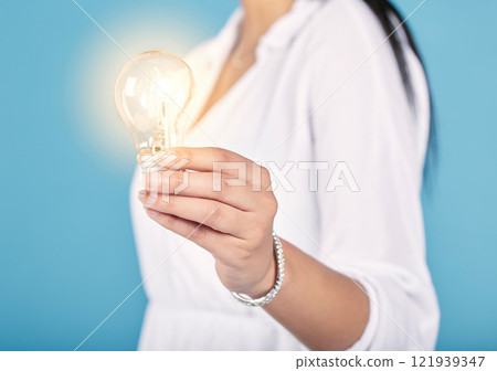 Lightbulb moment, idea and creativity with a light in the hand of a woman in studio isolated on a blue background. Closeup of motivation, innovation and development in energy, power and electricity 121939347