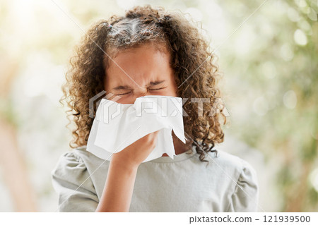 Sick little girl with a flu, blowing her nose and looking uncomfortable. Child suffering with sinus, allergies or covid symptoms and feeling unwell. Kid with a cold sneezing and holding a tissue 121939500