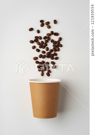 A paper coffee cup surrounded by freshly roasted coffee beans on a clean white background A paper coffee cup surrounded by freshly roasted coffee beans on a clean white background 121939554