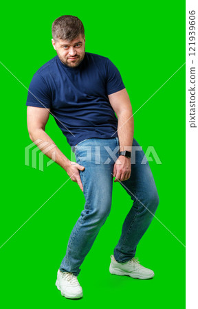 A man in a blue shirt and jeans awkwardly poses against a bright green backdrop 121939606