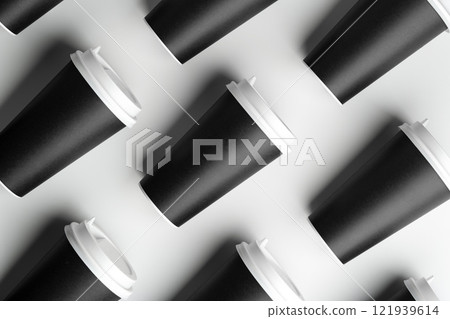 Multiple black takeaway coffee cups arranged in a repeating pattern on a white surface 121939614