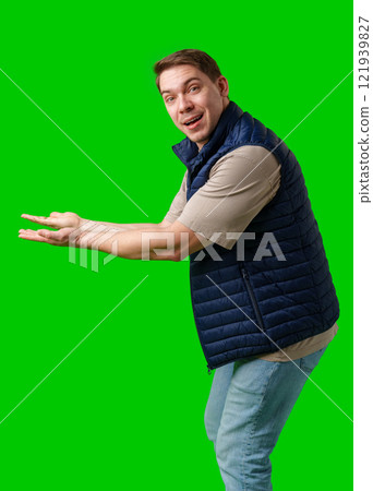 Man in a navy vest gestures enthusiastically toward a green screen 121939827